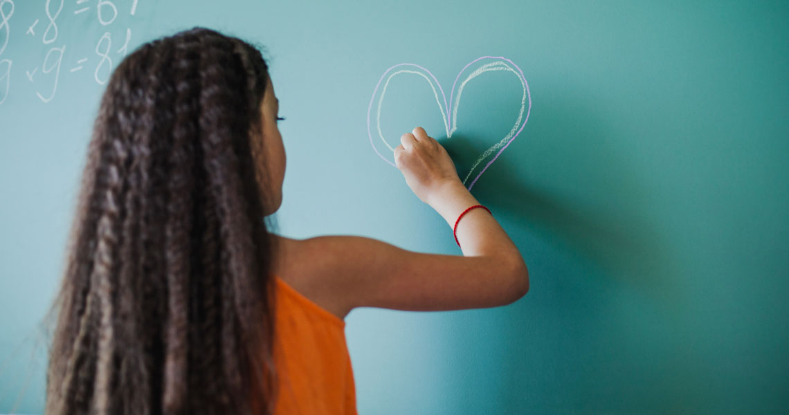 Niña dibujando un corazón en la pizarra