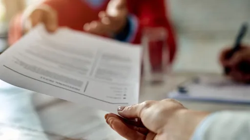 Persona entregant documentació a una altra en un despatx