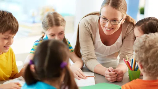 Infants amb educadora treballant en una aula somrients