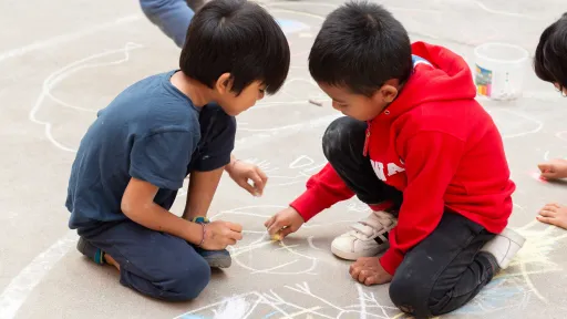 Nens al pati d'un centre socioeducatiu dibuixant amb guix
