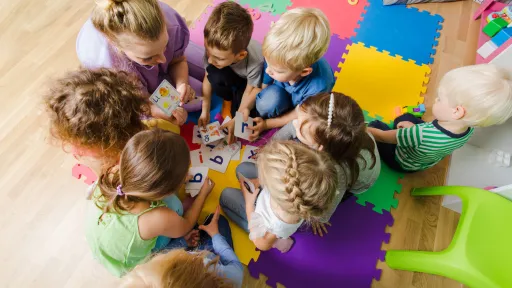 Professora al terra amb un grup de bebes mirant targetes amb lletres