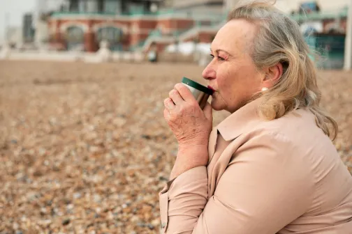 Dona gran amb un café a una platja