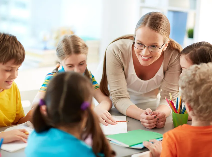Infants amb educadora treballant en una aula somrients
