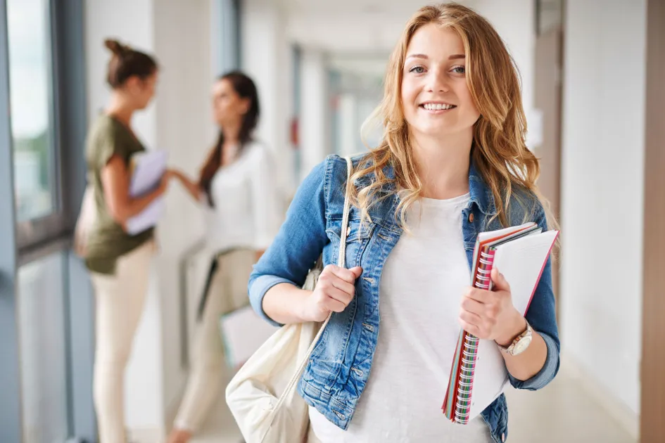 Noia amb una motxilla i llibretes al passadissos d'una universitat