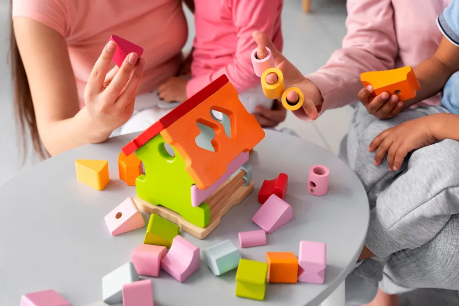 Professora amb dos bebes jugant amb una caseta de fusta