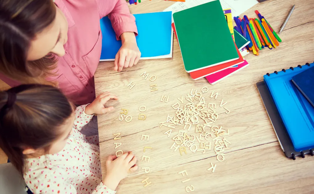 Professora amb una nena mirant lletres de fusta a una escola infantil