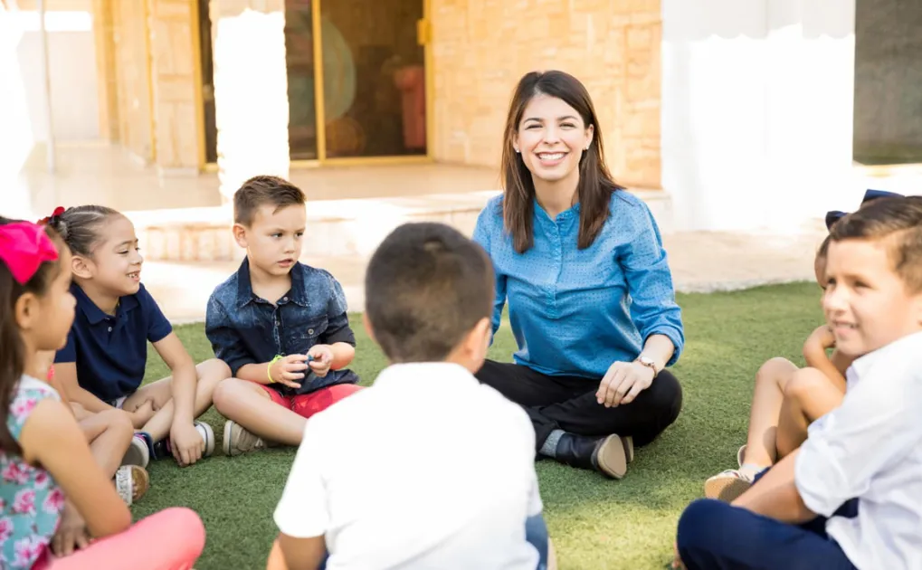 Professora amb infants en rotllana al pati d'una escola