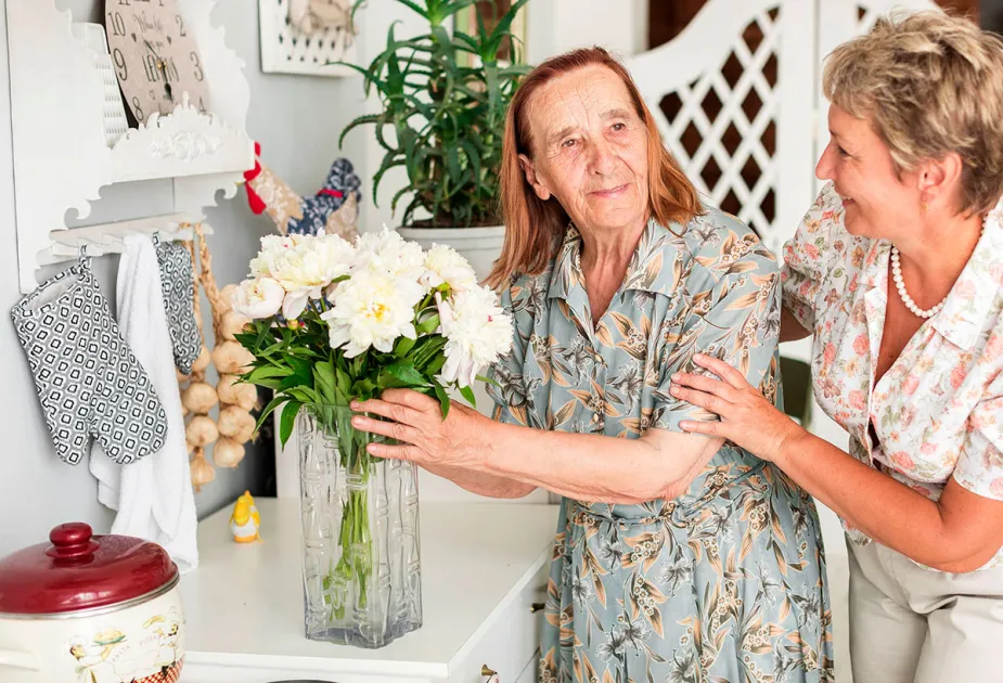 Dona i dona gran somrients a una cuina arreglant un gerro amb flors