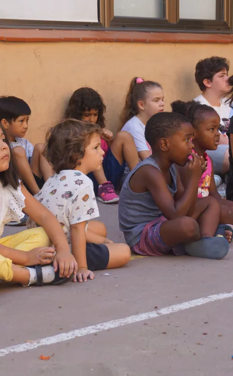 Grup d'infants en un casal d'estiu aseguts al pati amb una monitora