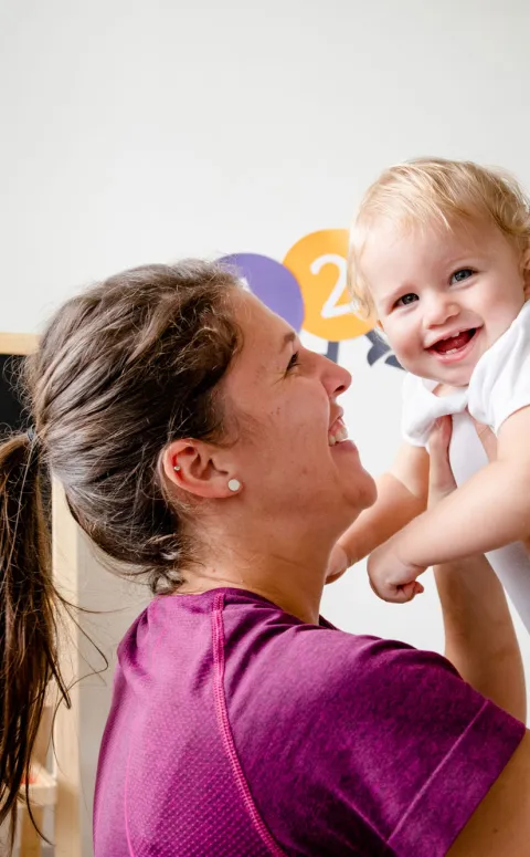 Professora somrient aixecant un bebe en una aula d'una escola infantil
